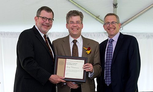 Gary Christenson poses with President Eric Kaler and Professor William Tolman, chair of the President's Award for Outstanding Service Committee. Christenson is holding his certificate.