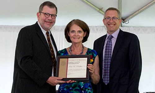 Kim R. Dockter poses with President Eric Kaler and Professor William Tolman, chair of the President's Award for Outstanding Service Committee. Dockter is holding her certificate.