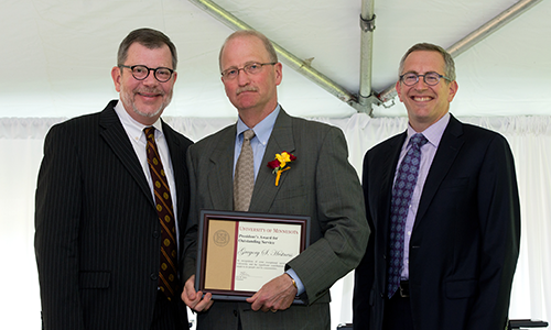 Gregory S. Hestness poses with President Eric Kaler and Professor William Tolman, chair of the President's Award for Outstanding Service Committee. Hestness is holding his certificate.