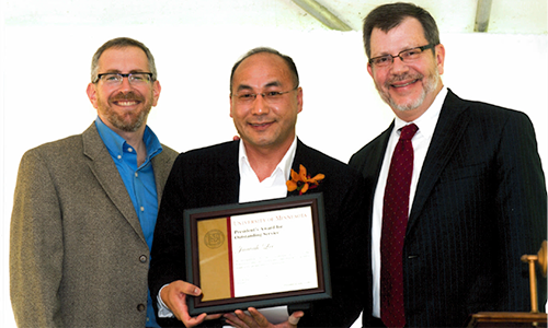 Juavah Lee poses with President Eric Kaler and Professor William Tolman, chair of the President's Award for Outstanding Service Committee. Lee is holding his certificate.