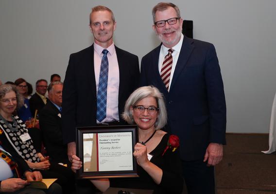 Tammy Berberi receiving award pictured with President Eric W. Kaler and Professor Robert Geraghty, chair, President's Award Committee